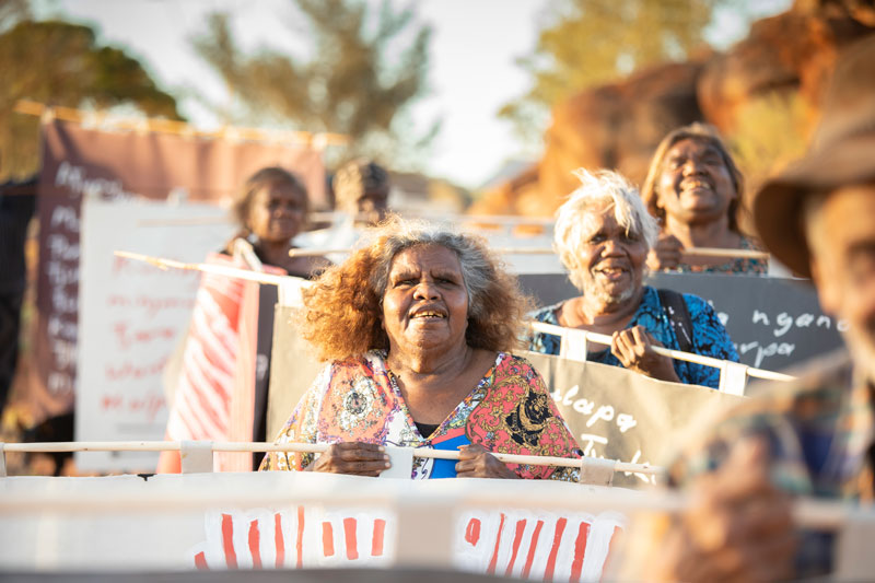 Tuppy Goodwin (centre) and other Mimili community members march with their banners for the Biennale of Sydney. Photo: Meg Hansen. Courtesy Mimili Maku Arts