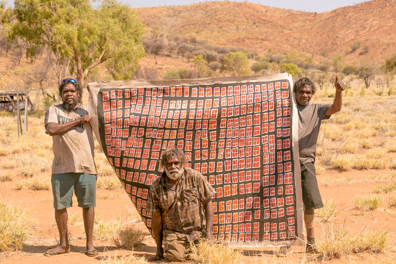 At the men’s painting camp in October 2018, Carbiene McDonald with his first work, together with Aaron Kingsley and Snowy McDonald. Courtesy Papunya Tjupi Arts, Papunya