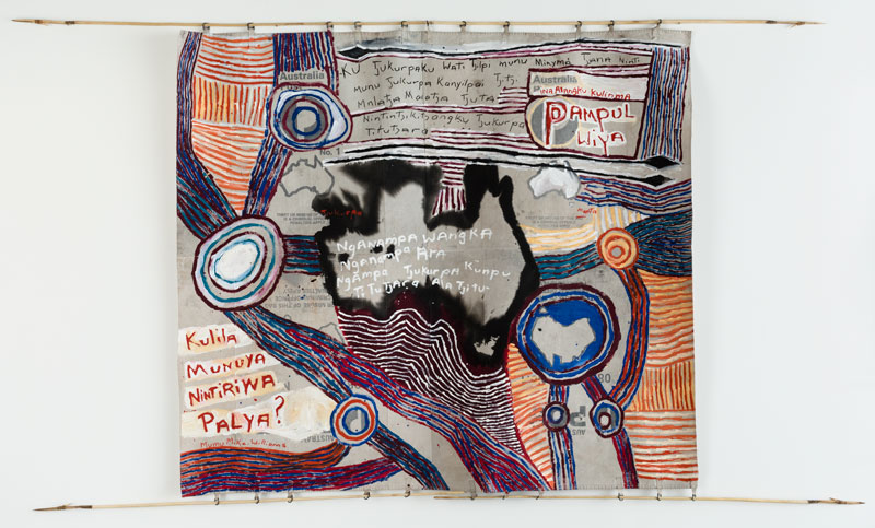 Mumu Mike Williams with Sammy Dodd (spears), Postbag Painting, 2017, synthetic polymer paint on canvas mailbag; wood, kangaroo tendon. Artbank collection, purchased 2017.  Text in English: Australia’s Tjukurpa is held and managed by our senior men and women.  They are the ones who are keeping our Tjukurpa strong for new generations  of children coming up, and will continue to teach it, always.  Australia, open your ears and remember this.  Do not damage our cultural heritage.  Theft or misuse of this Tjukurpa is a criminal offence. Penalties apply.  Theft or misuse of this land is a criminal offence. Penalties apply.  Our language, our cultural identity and our Tjukurpa are strong and enduring.  Listen and learn, okay?