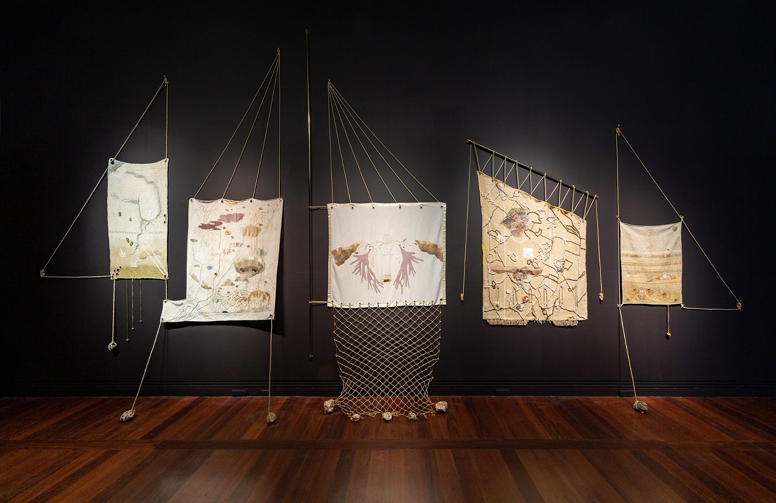 Art installation of cream-coloured sail cloth and ropes against black wall.