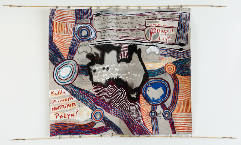 Mumu Mike Williams with Sammy Dodd (spears), Postbag Painting, 2017, synthetic polymer paint on canvas mailbag; wood, kangaroo tendon. Artbank collection, purchased 2017. Text in English: Australia’s Tjukurpa is held and managed by our senior men and women. They are the ones who are keeping our Tjukurpa strong for new generations of children coming up, and will continue to teach it, always. Australia, open your ears and remember this. Do not damage our cultural heritage. Theft or misuse of this Tjukurpa is a criminal offence. Penalties apply. Theft or misuse of this land is a criminal offence. Penalties apply. Our language, our cultural identity and our Tjukurpa are strong and enduring. Listen and learn, okay?