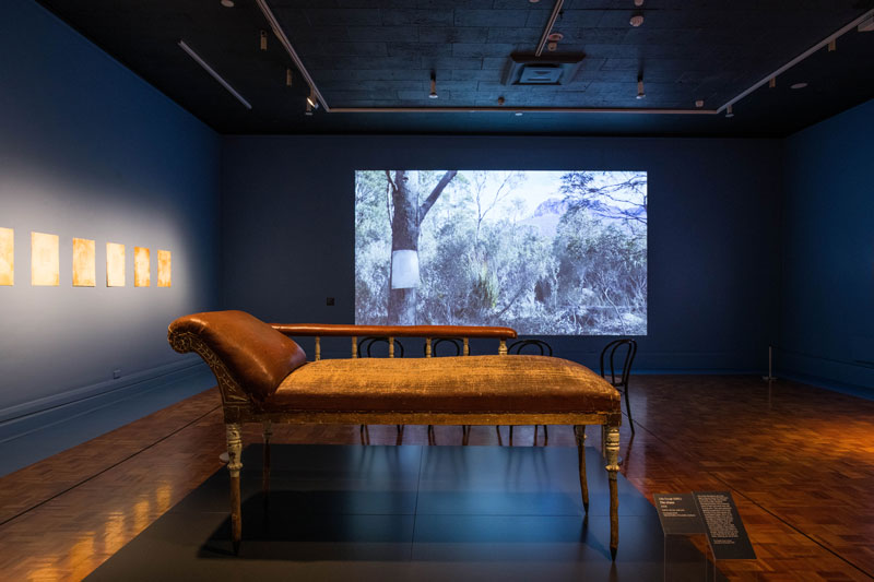(Front) Julie Gough, The Chase, 2008, leather, tea tree, steel pins. Collection National Gallery of Australia, Canberra; (Back) Hunting Ground (haunted), 2016–17, video, sound; (Left) Hunting Ground (haunted), 2016, etching and acrylic silkscreen, printed at Cicada Press, University of New South Wales. Installation view, Julie Gough: Tense Past, Tasmanian Museum and Art Gallery. Photo: Alastair Bett