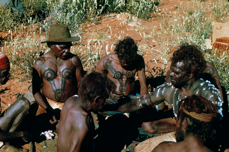 Left to right: Pinta Pinta Tjapanangka, Anatjari Tjampitjinpa, Charlie Ward Tjakamarra (in foreground), Anatjari Tjakamarra, unknown (obscured), Willy Tjapanangka, unknown (back of head) prepare for a performance